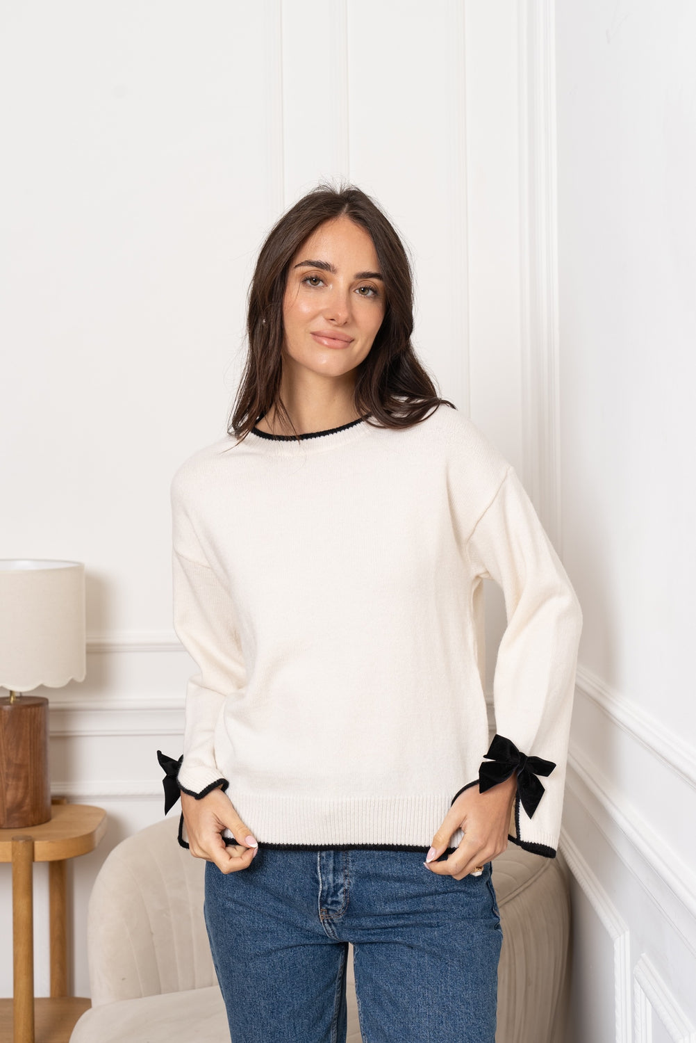 Maglioncino ecru in morbida maglia con bordi neri a contrasto e fiocchi di velluto sui polsini, ideale per un look elegante e femminile.