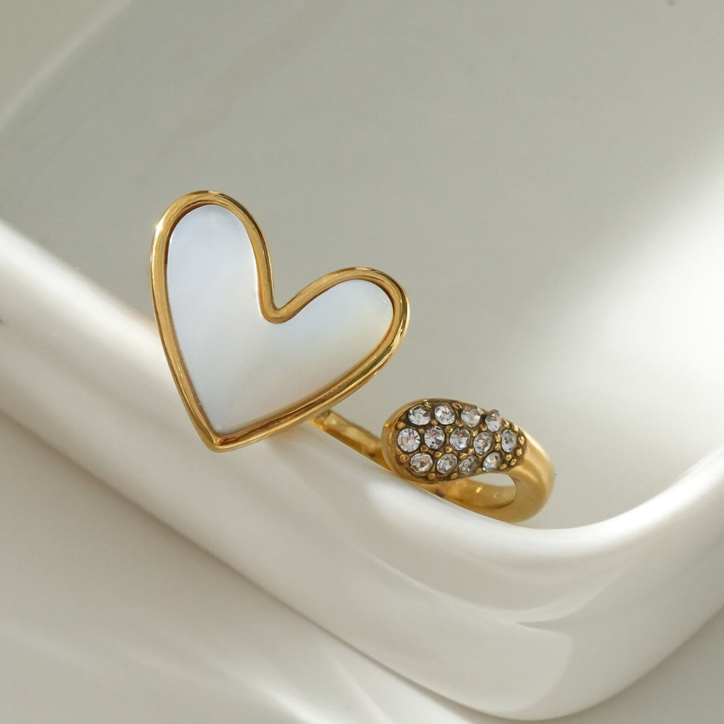 Anello dorato con cuore in madreperla bianca e cristalli decorativi.